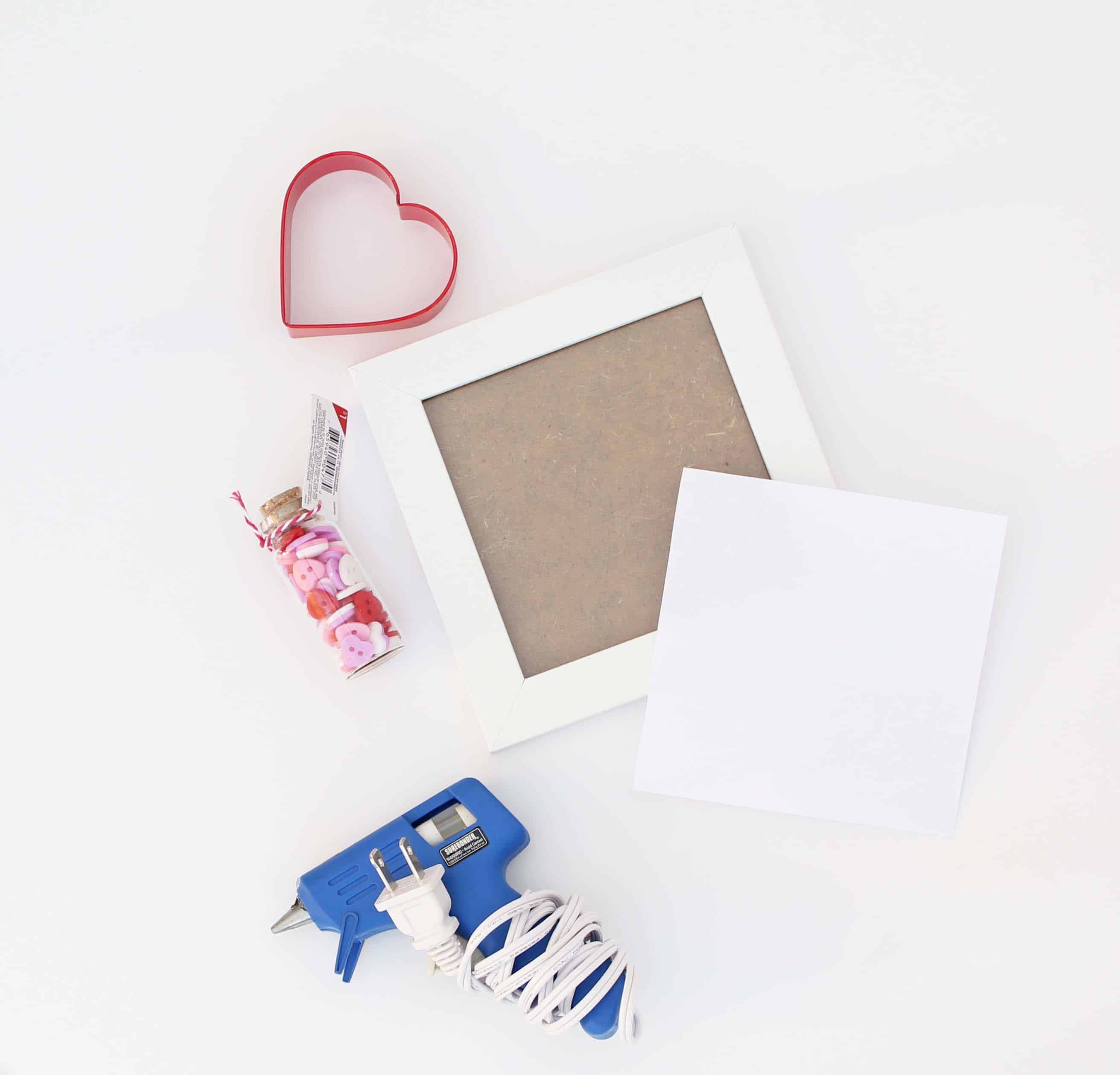 red heart cookie cutter, glue gun, white picture frame, jar of heart buttons