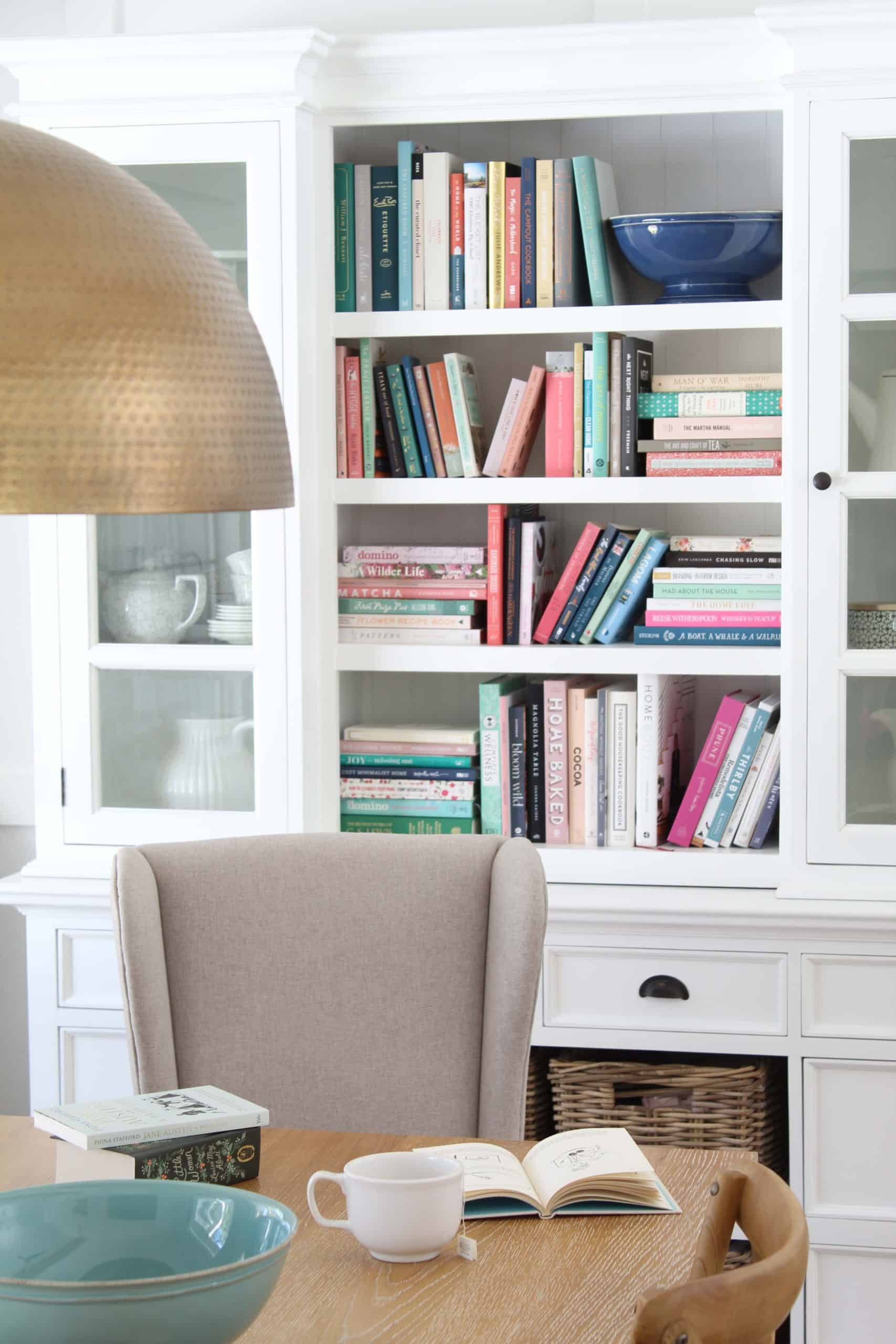 colorful books on bookshelf, brass dining pendant light, large white book case hutch