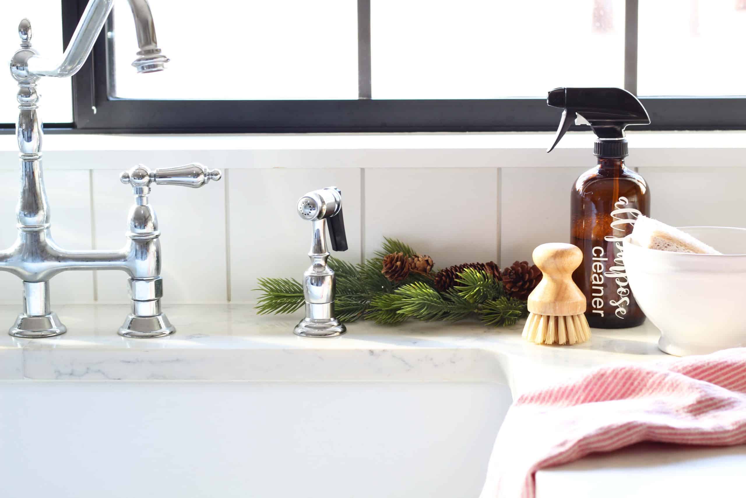 amber all purpose cleaning bottle, kingston chrome bridge faucet, white farmhouse sink , black kitchen windows with farmhouse sink