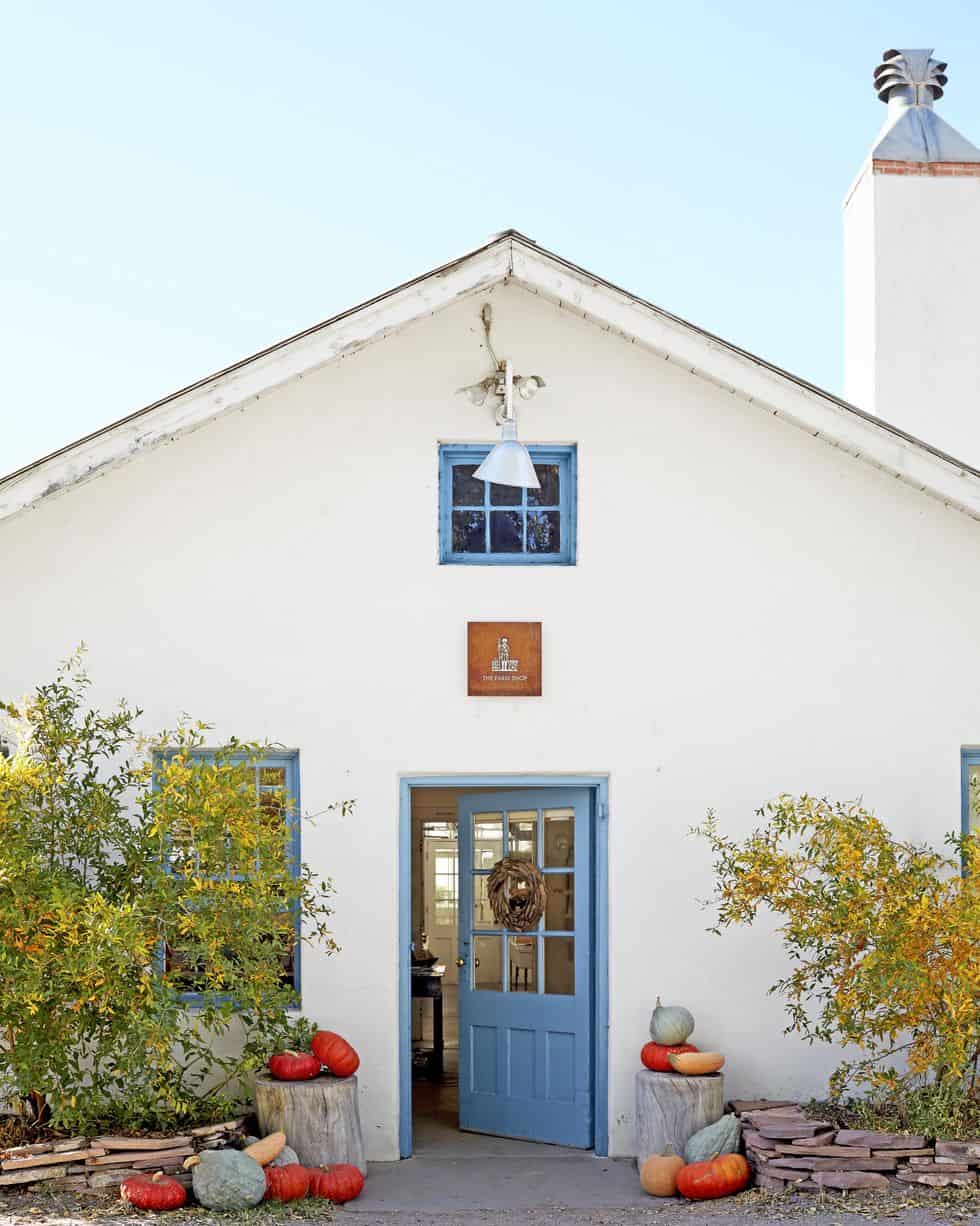 white cottage with blue door and pumpkins sitting on tree stumps