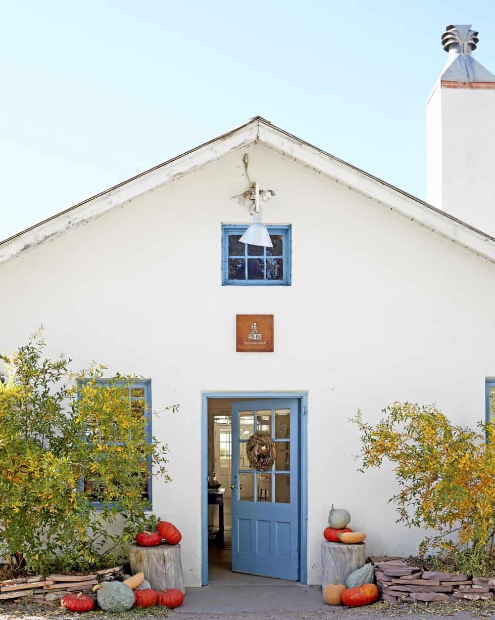 white cottage with blue door and pumpkins sitting on tree stumps