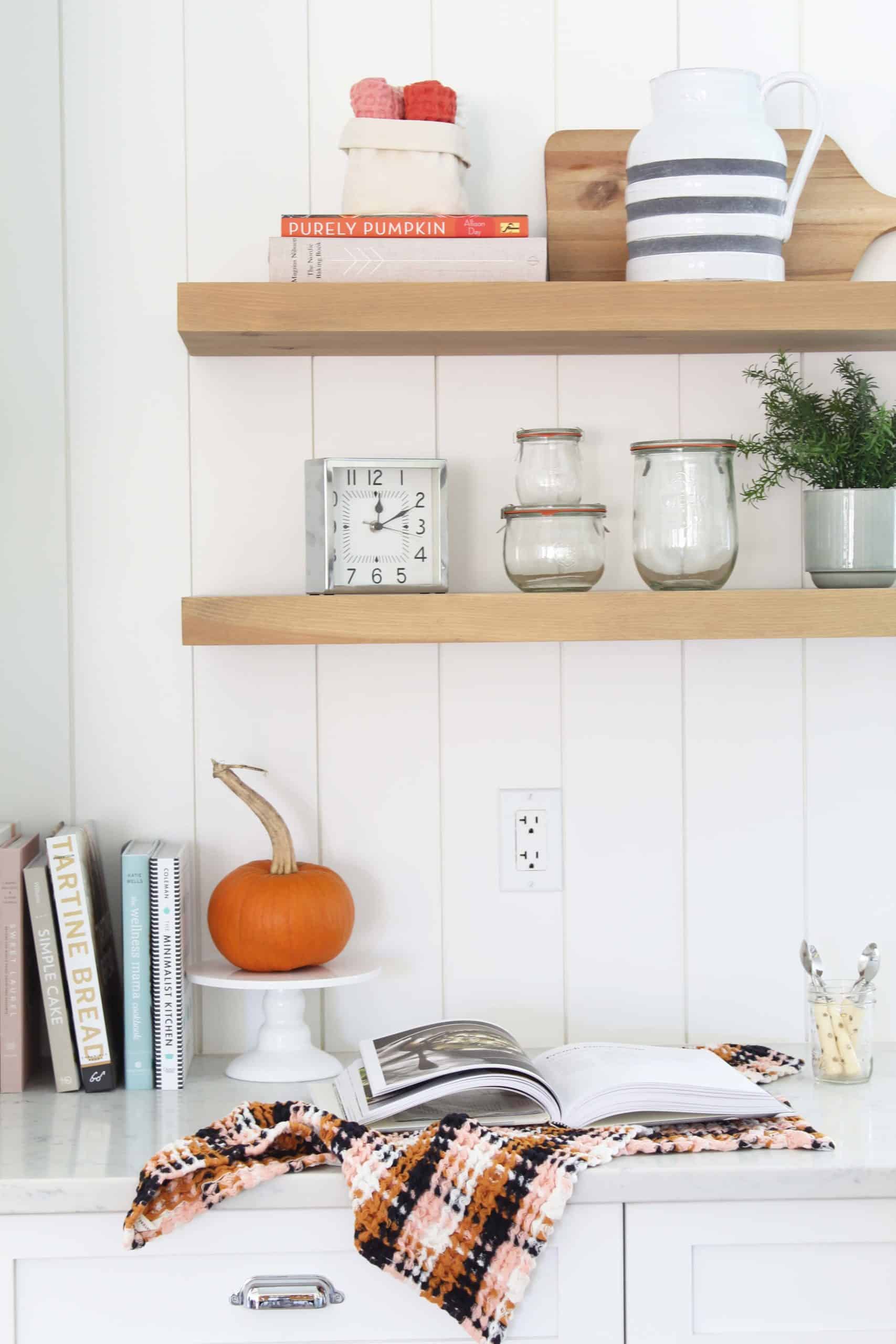 open kitchen shelving with wreck tulip jars, anthropologie dish cloths and striped pitcher, and pumpkin